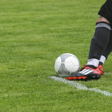 Soccer Player Kicking White Gray Soccer Ball on Green Grass Field